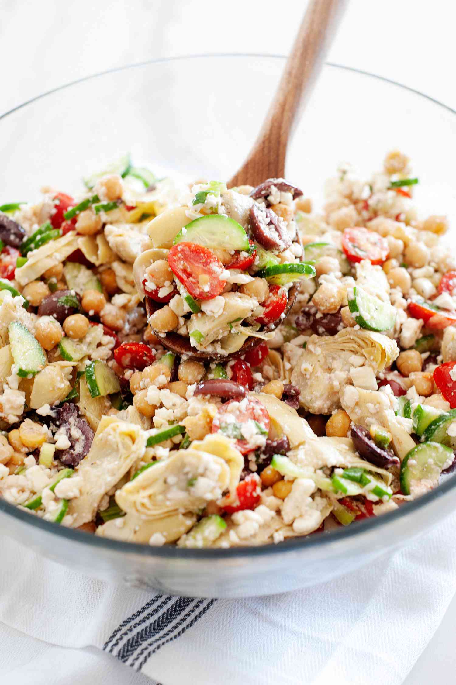 The best Mediterranean chickpea salad in a glass serving bowl with a wooden spoon inside.