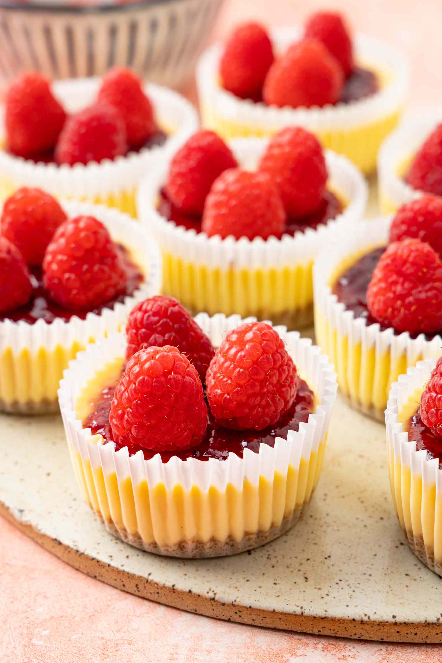 Mini Cheesecakes Wrapped in Cupcake Wrappers and Topped With Jam and Raspberries, All on a Stone Platter 