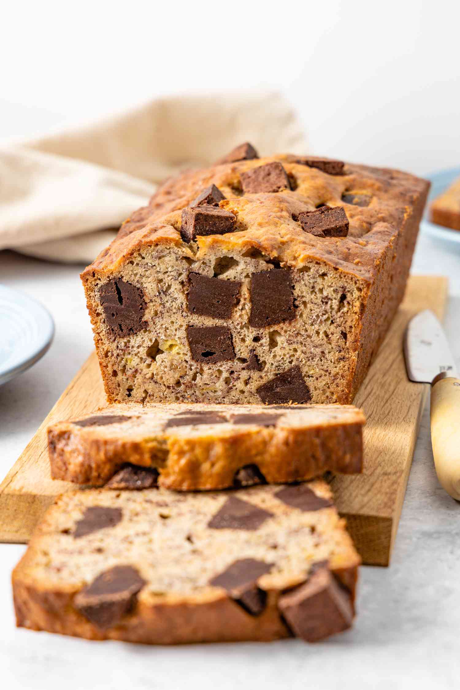 On a Wooden Board, Loaf of Brownie Banana Bread with Slices Cut Off, and in the Surroundings, a Plate and a Kitchen Towel