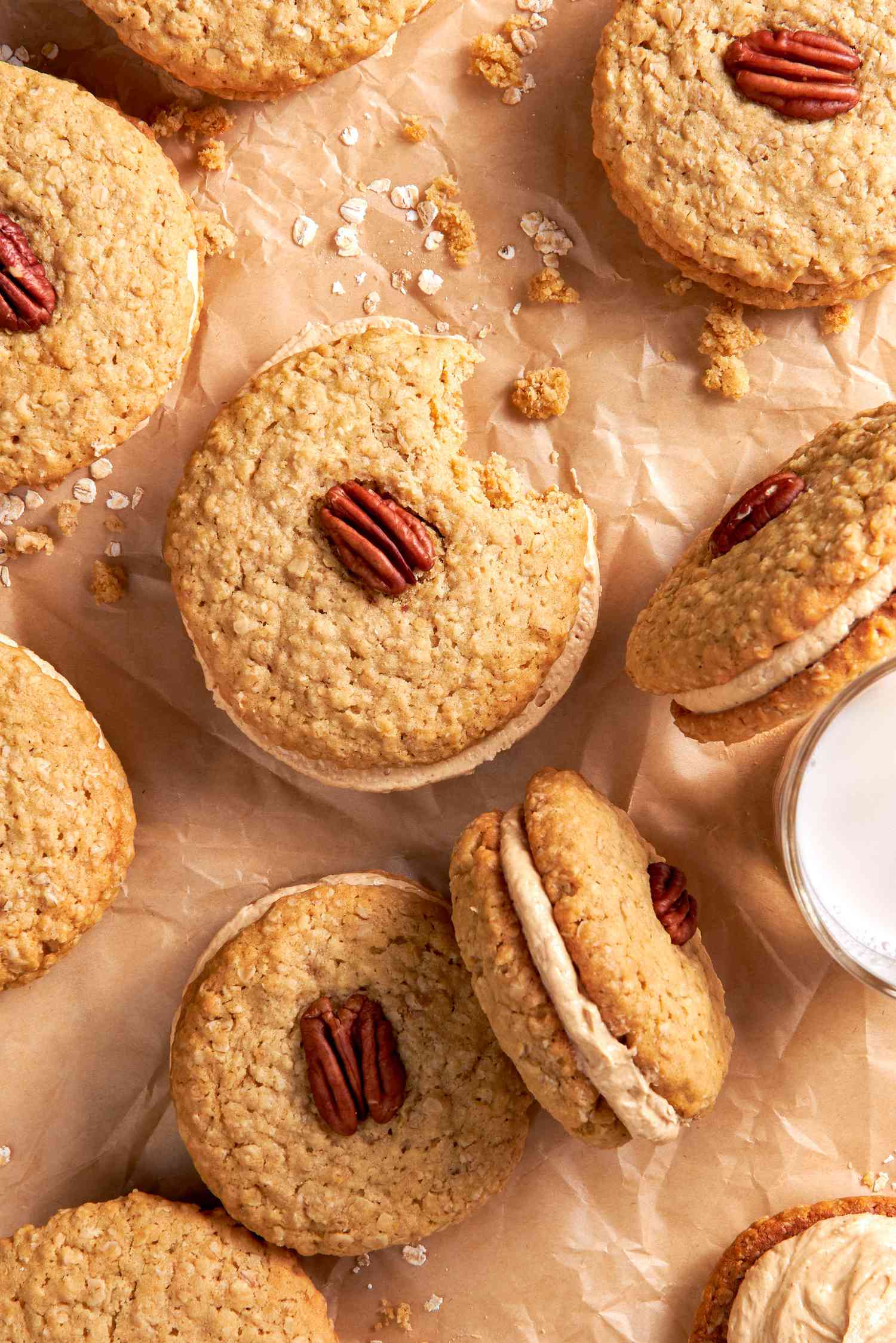 Yellowhammer cookies (one is missing a bite) on a piece of parchment paper with some oats and crumbs around the cookies and a glass of milk