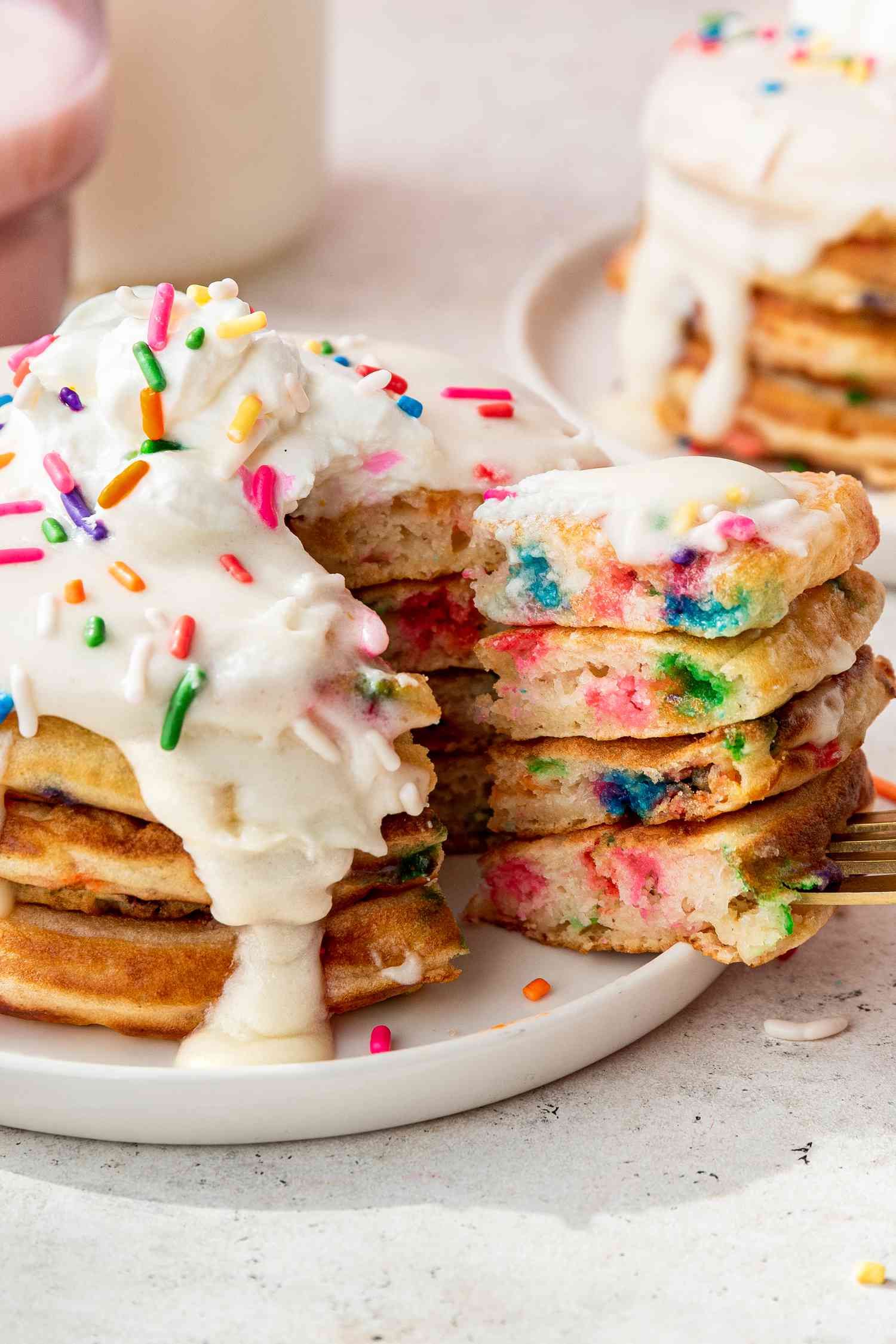 Slice of Stacked Funfetti Pancakes Removed From Plate With the Rest of the Pancake Using a Fork, and in the Surroundings, Another Stack in the Background, and a Glass of Milk