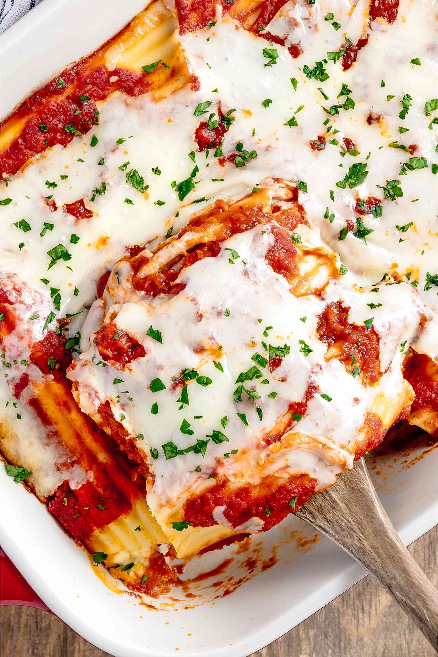Manicotti Removed From Casserole Dish Filled With Manicotti Using a Wooden Spoon