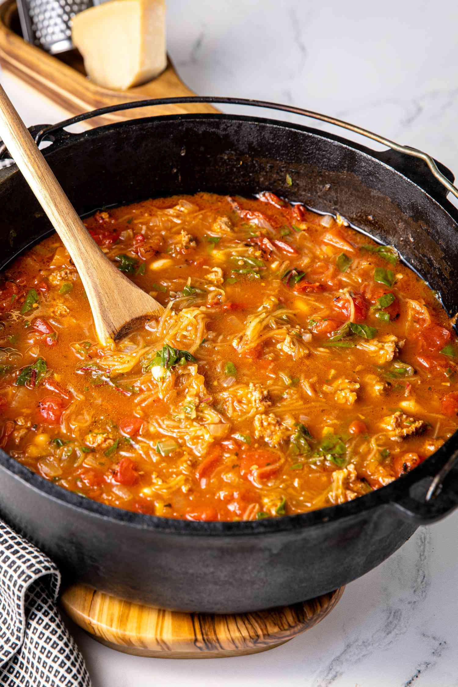 Spaghetti Squash Soup with Italian Sausage in a Cast Iron Pot with a Spoon in It, Resting on a Wooden Slab