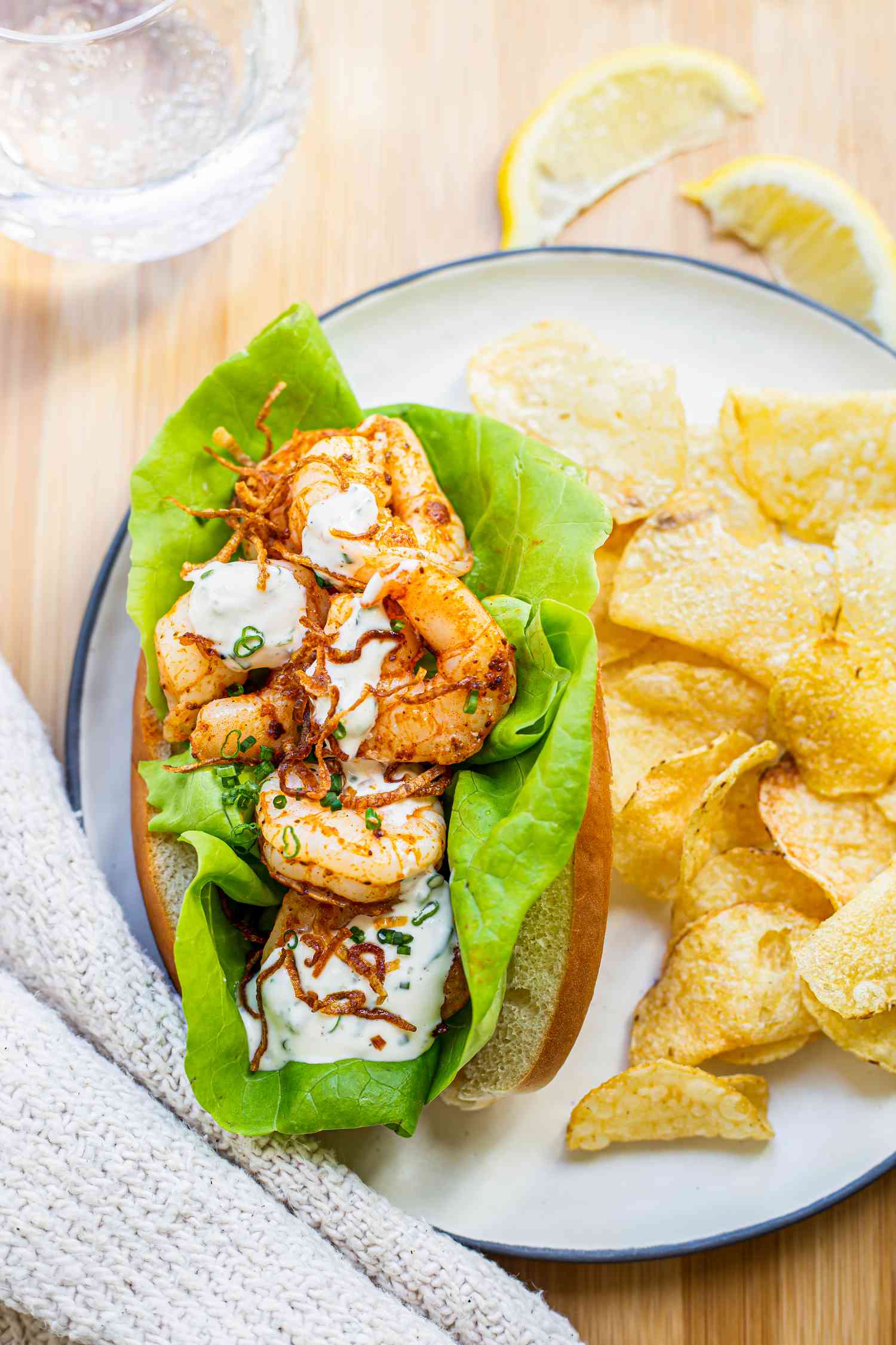 Old Bay Shrimp Rolls on a Plate with Chips Next to a Drink, Lemon Wedges on Table, and a Cloth Napkin