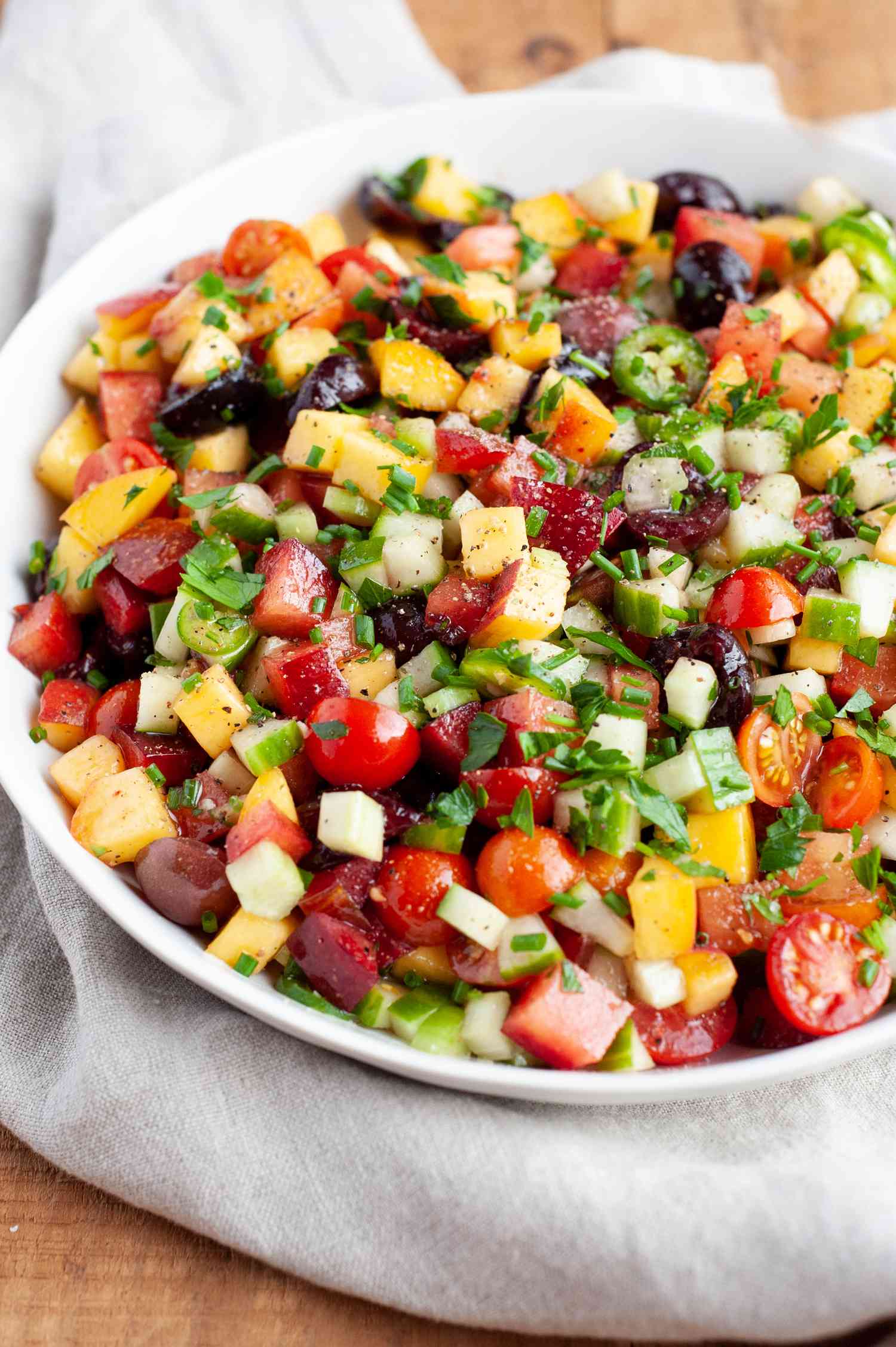 Stone fruit and vegetable salad in a serving bowl with a linen underneath.