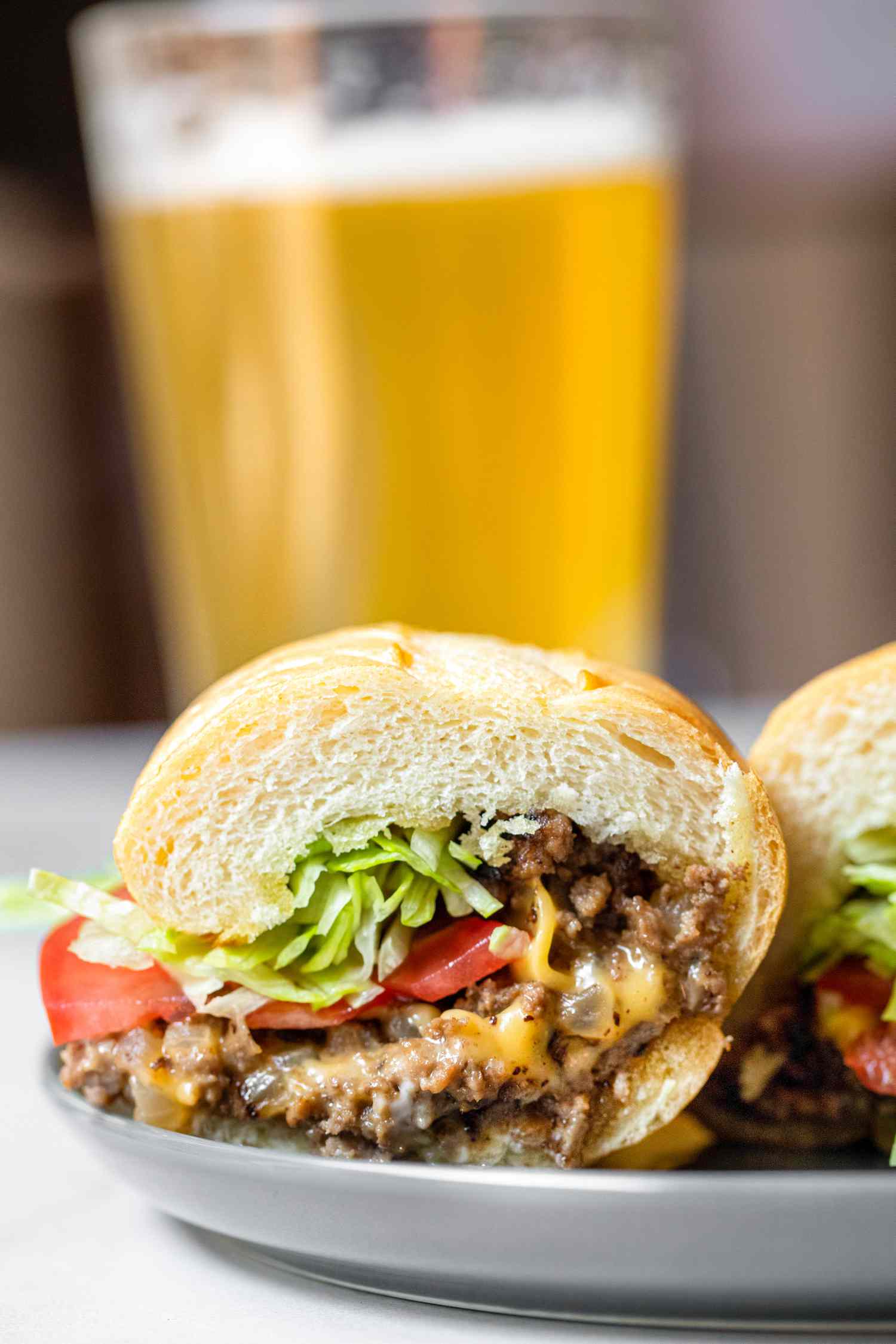 Two Halves of a Chopped Cheese Sandwich and a Pickle on a Plate, and in the Background, a Drink-Filled Glass
