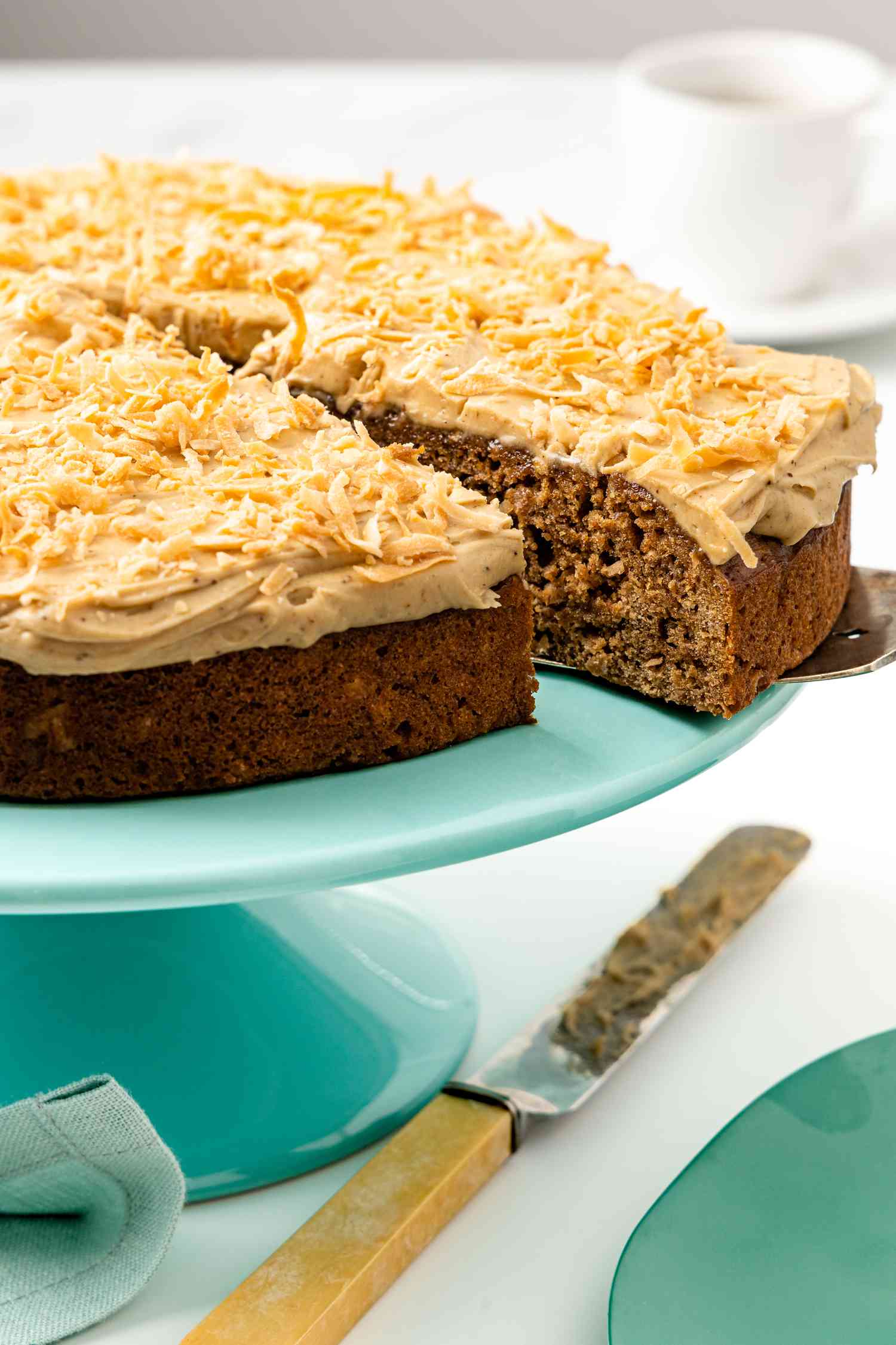 Coffee Coconut Banana Bread Cake on a Cake Platter With a Cut Slice Being Removed Using a Pie Server